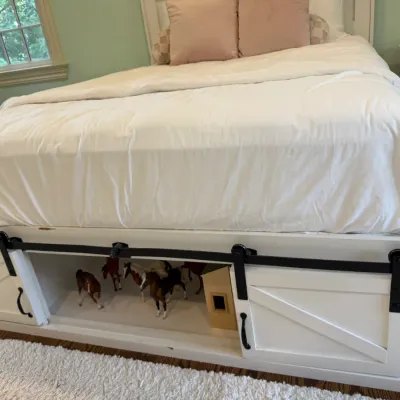 Sale Photo Thumbnail #167: White farmhouse-style bed frame with built-in under-bed storage behind sliding barn doors, displayed with model horse figurines inside.