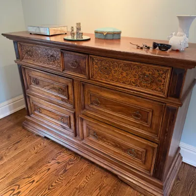 Sale Photo Thumbnail #90: Vintage Mediterranean-style wooden triple dresser featuring intricately carved upper drawer fronts and brass bail handles.