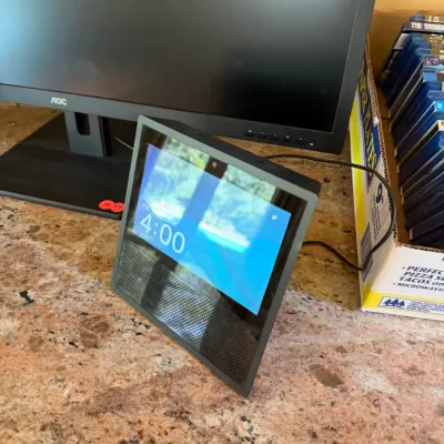 Sale Photo Thumbnail #184: Amazon Echo Show 1st generation smart display unit, powered on and displayed alongside an AOC computer monitor.