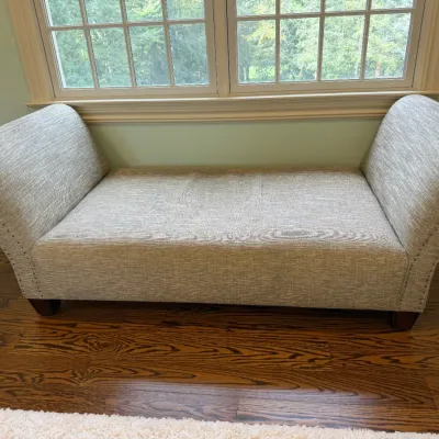 Sale Photo Thumbnail #162: Contemporary upholstered bench with rolled arms and nailhead trim, featuring textured light gray fabric and dark wood feet.