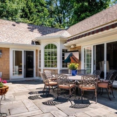 Sale Photo Thumbnail #13: Outdoor patio dining set featuring a large oval table with an ornate lattice pattern and matching armchairs with orange seat cushions, set on a stone flagstone patio.