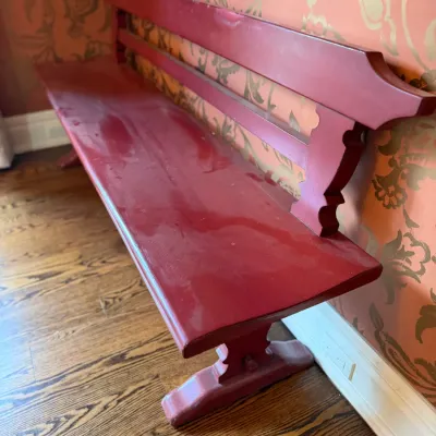 Sale Photo Thumbnail #195: Vintage long wooden deacon's bench painted in a dark red finish, featuring decorative shaped side supports and a slatted backrest.