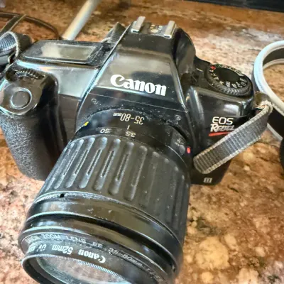 Sale Photo Thumbnail #187: Canon EOS Rebel II 35mm SLR camera fitted with a Canon EF 35-80mm zoom lens, showing noticeable dust and surface wear from light use.