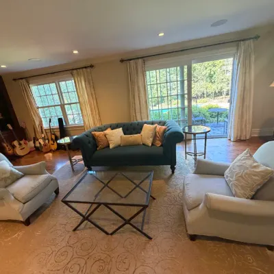 Sale Photo Thumbnail #26: Spacious living room set including a teal tufted Chesterfield sofa, a pair of light grey upholstered armchairs, a glass-top coffee table, and an patterned area rug.