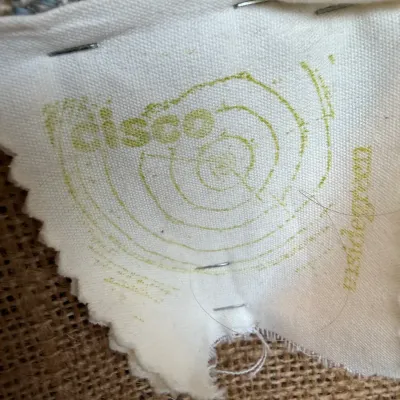 Sale Photo Thumbnail #163: Close-up of a Cisco Home fabric brand tag stapled to woven upholstery fabric.