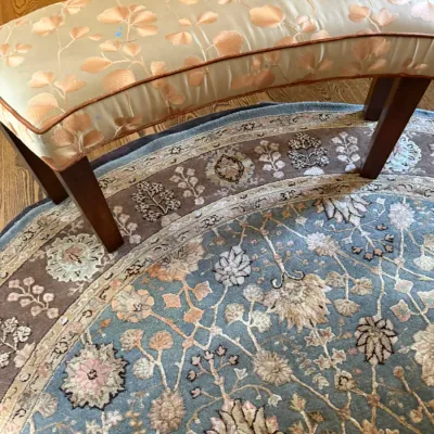 Sale Photo Thumbnail #75: Curved upholstered bench with a peach and gold botanical patterned fabric and dark wooden legs, set over a round ornate oriental rug.