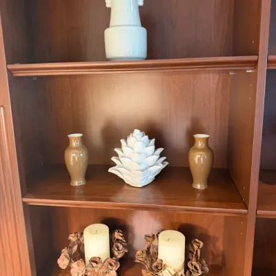 Sale Photo Thumbnail #45: A wooden bookcase displaying a white ceramic vase, a pinecone-shaped centerpiece flanked by matching tan vases, and a pair of decorative candle holders.