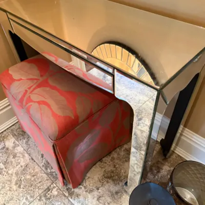 Sale Photo Thumbnail #113: Mirrored console desk featuring clean lines and bevel-edged mirrored paneling, paired with an upholstered pink-and-gold leaf pattern vanity stool.
