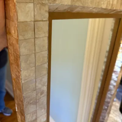 Sale Photo Thumbnail #204: Close-up of a wall mirror with a wide frame featuring iridescent mother-of-pearl or capiz shell mosaic tiles and a gold inner lip.