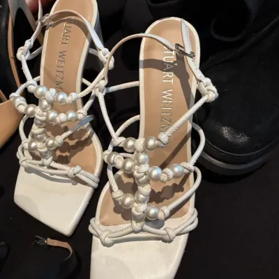 Sale Photo Thumbnail #103: Pair of Stuart Weitzman white strappy heel sandals featuring faux pearl embellishments along the knotted straps and square toes.