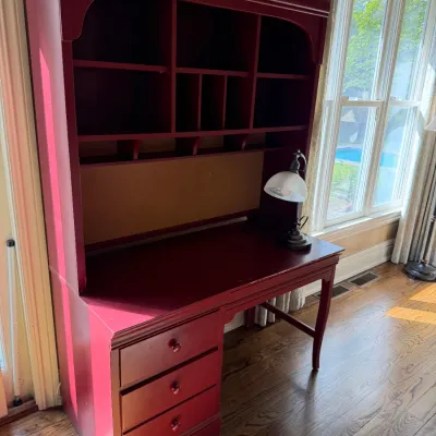 Sale Photo Thumbnail #175: Burgundy painted writing desk with an attached upper hutch featuring multiple cubbies and drawers, paired with a small desk lamp.
