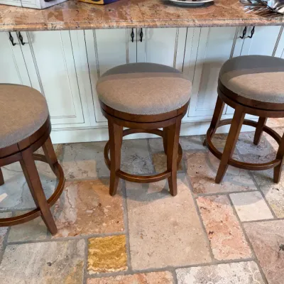 Sale Photo Thumbnail #134: Set of three transitional backless swivel barstools featuring dark wood frames and beige upholstered seats.