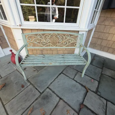 Sale Photo Thumbnail #24: Weathered mint green metal garden bench featuring a pineapple and scrollwork motif backrest, situated on a flagstone patio.