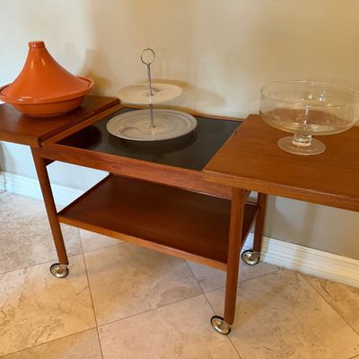 Sale Photo Thumbnail #4: Mid-century Danish modern teak rolling bar cart with sliding expanders, featuring a terracotta tagine, tiered server, and clear glass bowl displayed on top.