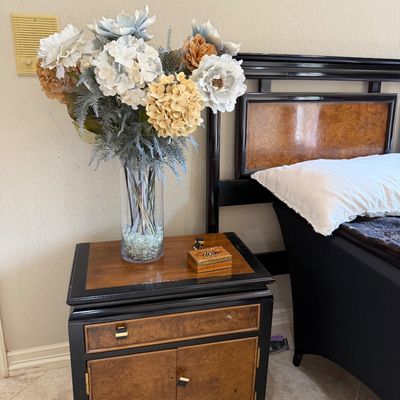 Sale Photo Thumbnail #26: Two-tone burl wood and black trim nightstand with a single top drawer and lower two-door cabinet, shown alongside a matching bed frame.