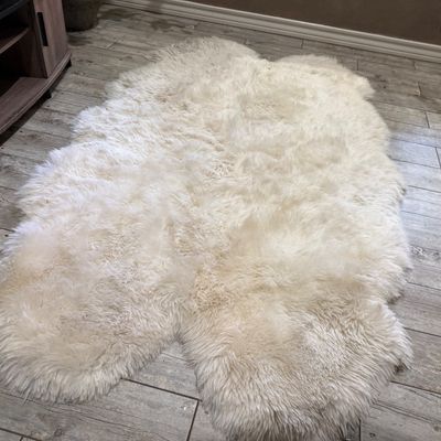 Sale Photo Thumbnail #74: Large ivory sheepskin rug laid out on tile flooring, featuring plush, high-pile fur and a multi-pelt shape.