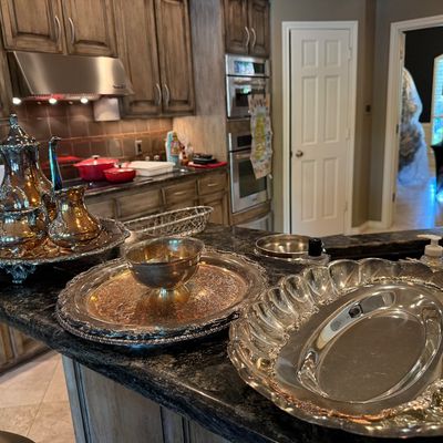 Sale Photo Thumbnail #46: Collection of silver-plated serving items, including a tea set on a footed tray, engraved round trays, a bowl, and a fluted oval platter arranged on a kitchen island.