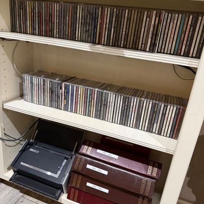 Sale Photo Thumbnail #76: White wooden bookcase filled with two shelves of music CDs in jewel cases, leather-bound photo albums, and a portable document scanner.