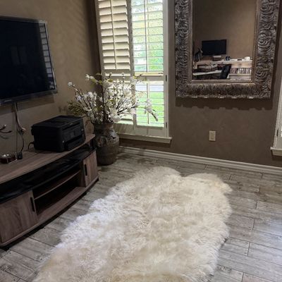 Sale Photo Thumbnail #73: Large white sheepskin rug displayed on a wood-look tile floor alongside a modern grey media console and an ornate ornate-frame wall mirror.