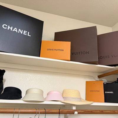 Sale Photo Thumbnail #22: Collection of luxury designer gift boxes and shopping bags including Chanel and Louis Vuitton, displayed alongside various hats and a pair of black boots on closet shelves.