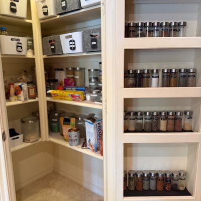 Sale Photo Thumbnail #13: Walk-in pantry featuring built-in shelving, organized storage bins with labels, and a door-mounted spice rack filled with matching glass spice jars.