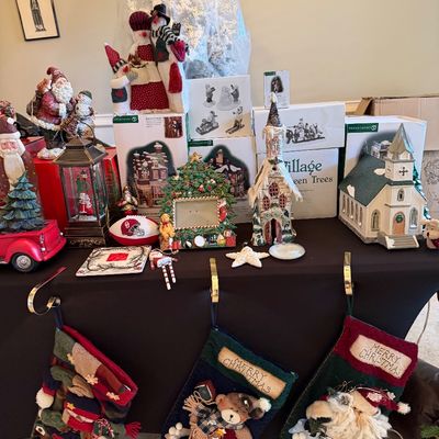 Sale Photo Thumbnail #5: Collection of Christmas decorations including Department 56 village buildings, fabric stockings hanging from stocking holders, plush snowmen, figurines, and holiday boxes.