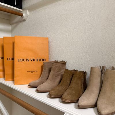 Sale Photo Thumbnail #21: Collection of women's suede ankle boots in tan and neutral tones, displayed on a shelf alongside orange Louis Vuitton and black Chanel shopping bags.