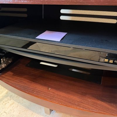Sale Photo Thumbnail #83: Sony 4K Ultra HD Blu-ray player with high-res audio capability, resting inside a dark wood media cabinet shelf.