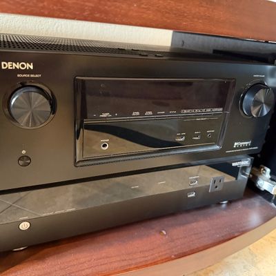 Sale Photo Thumbnail #80: Denon IN-Command Series integrated network AV receiver sitting atop a WattBox power conditioner inside a dark wood audio cabinet.