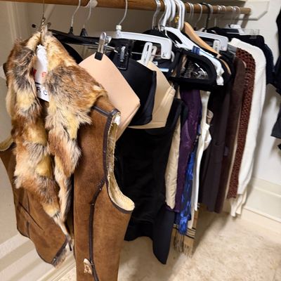 Sale Photo Thumbnail #20: A rack of women's clothing, featuring a vintage shearling and faux fur trim vest alongside various tops and bras.