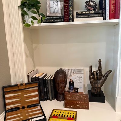 Sale Photo Thumbnail #77: Collection of home decor items and games displayed on built-in shelving, including a leatherette backgammon set, mini chess set, carved wooden head sculpture, inlaid wooden box, and books.