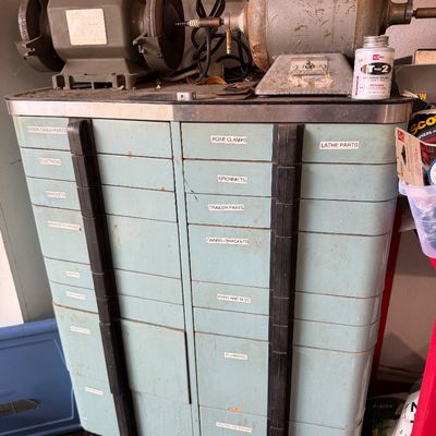 Sale Photo Thumbnail #102: Vintage light blue metal parts organizer cabinet with labeled drawers, topped with two electric bench grinders and workshop supplies.