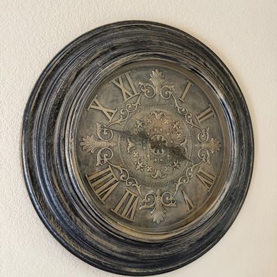 Sale Photo Thumbnail #35: Large antique-style circular wall clock featuring a distressed dark wood frame and an ornate embossed metallic face with Roman numerals.