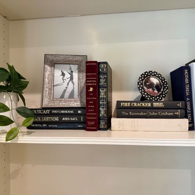 Sale Photo Thumbnail #82: Collection of hardback books displayed on a shelf alongside framed photos and a potted green plant.
