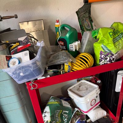 Sale Photo Thumbnail #71: Red metal utility cart holding an assortment of garden care supplies, lawn fertilizers, pest control sprays, and coiled yellow hose.