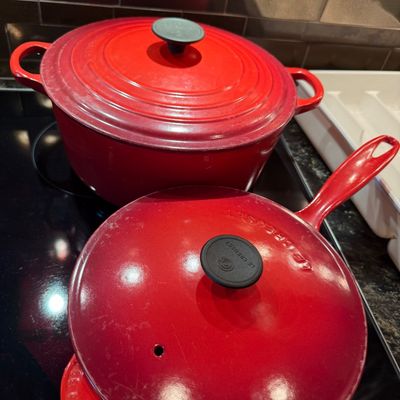 Sale Photo Thumbnail #16: Two red Le Creuset enamel-coated cast iron cookware pieces, including a Dutch oven and a covered saucepan or skillet, showing minor surface wear from use.