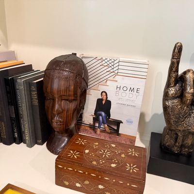 Sale Photo Thumbnail #78: A collection of decorative objects including a carved wood head sculpture, an inlaid wooden trinket box, a bronze-style hand gesture sculpture, and various books.