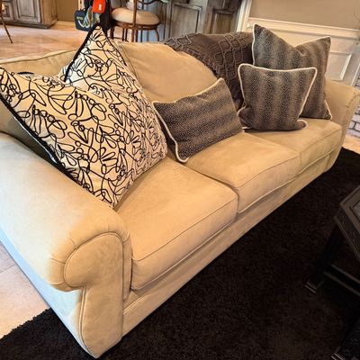 Sale Photo Thumbnail #40: Contemporary beige rolled-arm sofa, upholstered in microfiber or faux suede, styled with decorative throw pillows and a knit blanket.