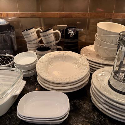 Sale Photo Thumbnail #47: Collection of white ceramic dinnerware with embossed leaf details, black and white striped mugs, a glass French press, and small appliances on a kitchen counter.