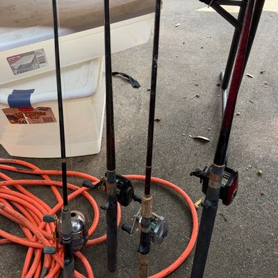 Sale Photo Thumbnail #97: Collection of four fishing rods with attached spincast and baitcasting reels leaning against a table.