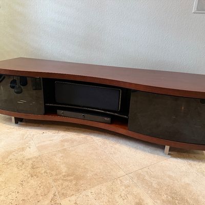 Sale Photo Thumbnail #81: Modern curved wood media console featuring tinted glass cabinet doors, open central shelving, and sleek metal feet.