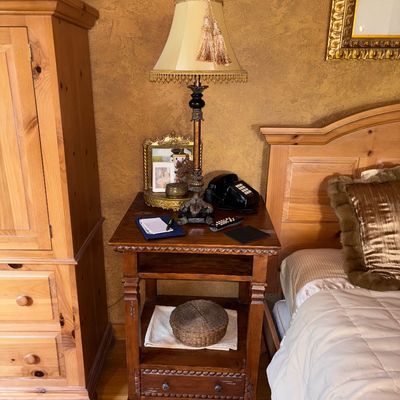 Sale Photo Thumbnail #45: Dark stained wooden nightstand with carved rope trim, topped with a traditional table lamp featuring fringe and tassels, flanked by a pine armoire and matching bed frame.