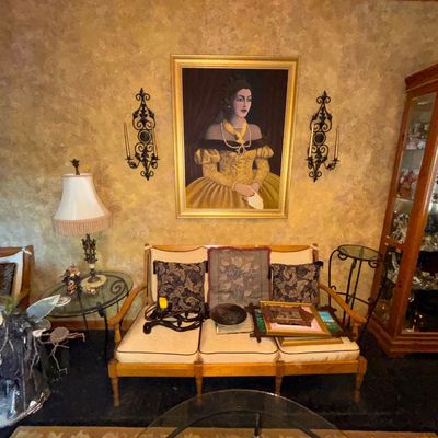 Sale Photo Thumbnail #84: Living room setup featuring a wooden three-cushion sofa, a large framed oil painting portrait of a woman in a gold dress, wrought iron wall sconces, and surrounding accent furniture.