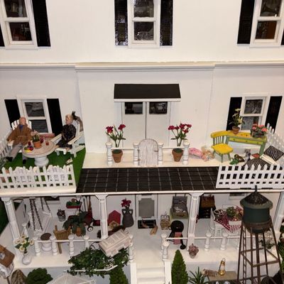 Sale Photo Thumbnail #19: Detailed multi-story dollhouse featuring white exterior siding, black shutters, porch railing, and various miniature figures and furniture pieces.