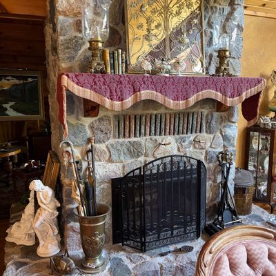 Sale Photo Thumbnail #13: Stone fireplace hearth display featuring a ornate brass umbrella stand with walking canes, a three-panel black mesh fire screen, a neoclassical white maiden statue, and an elaborate gold filigree mantle mirror with glass hurricane lamps.