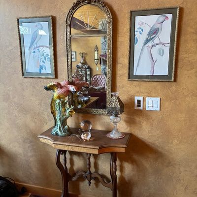 Sale Photo Thumbnail #18: Traditional wooden console table displayed with an ornate gilded arch mirror, framed bird prints, a colorful ceramic parrot figurine, and decorative accessories.