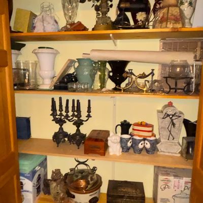 Sale Photo Thumbnail #92: Closet shelves filled with eclectic collectibles, including vintage vases, dark metal candelabras, a Jack Skellington figure, small kitchen appliances, and decorative boxes.