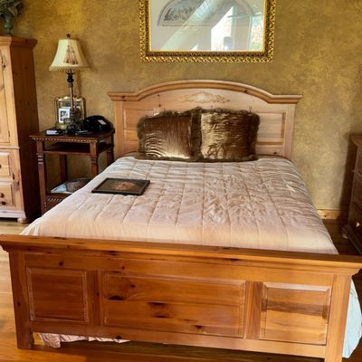 Sale Photo Thumbnail #48: Traditional knotty pine bed set including a queen-size bed frame, matching nightstand, and large ornate framed artwork mounted on textured walls.