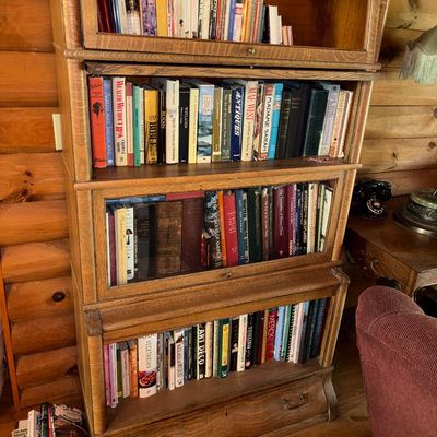 Sale Photo Thumbnail #24: Four-tier antique oak barrister bookcase filled with various hardback books, featuring glass lift-up doors and a bottom storage drawer.