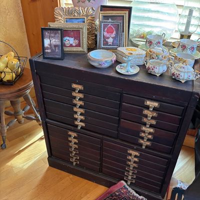 Sale Photo Thumbnail #67: Vintage dark wood multi-drawer flat file or printer's cabinet with metal label pulls, displayed alongside framed art pieces and floral porcelain tea sets.